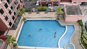 Vista aerea di una piscina circondata da un edificio a più piani con balconi, palme e una piccola fontana.