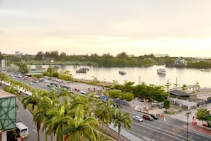 A waterfront view with a road, palm trees, and boats on the water.