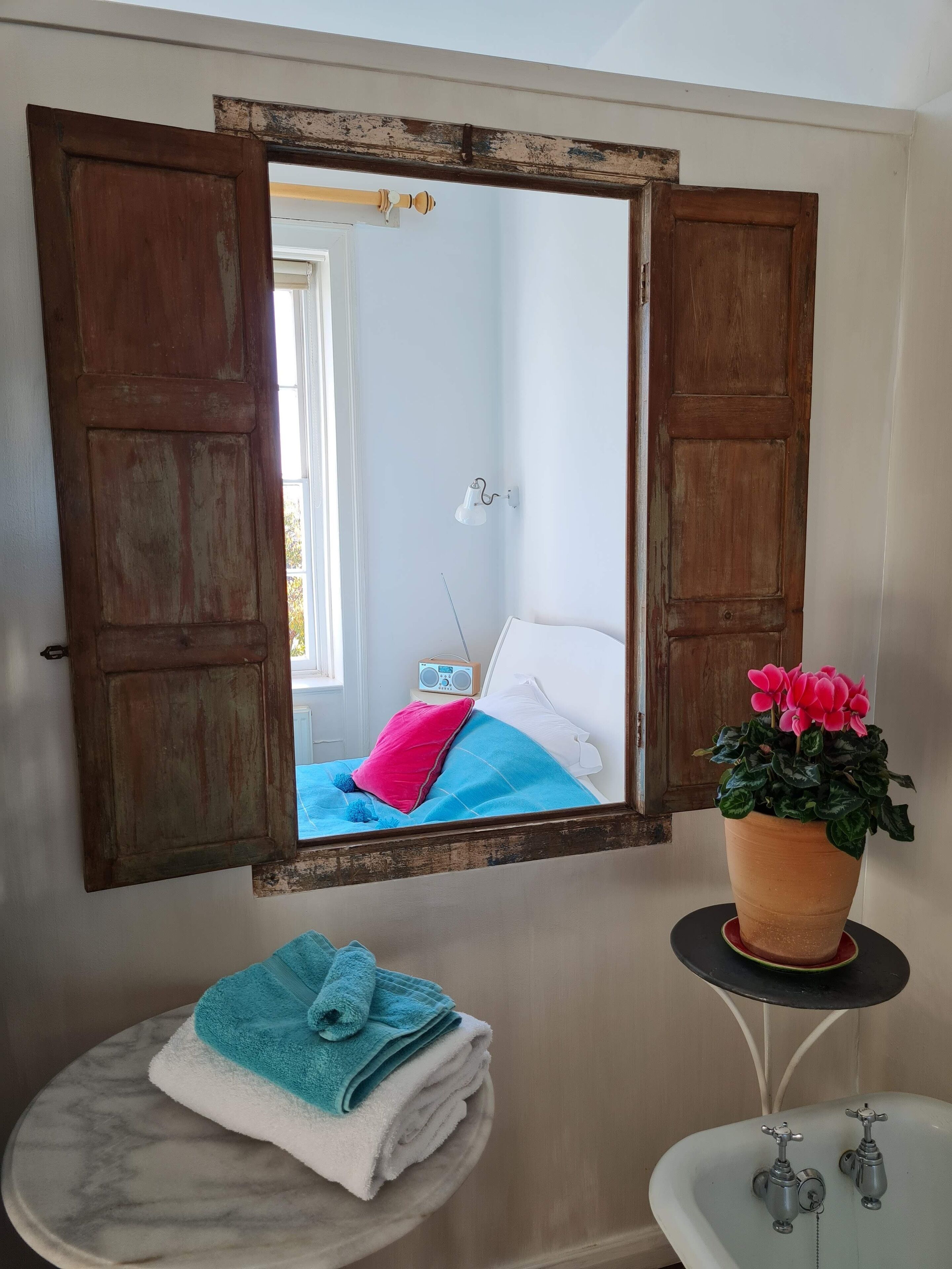 A bathroom with a marble sink, two faucets, a mirror with wooden frames, a potted plant, and a towel on a round marble table.
