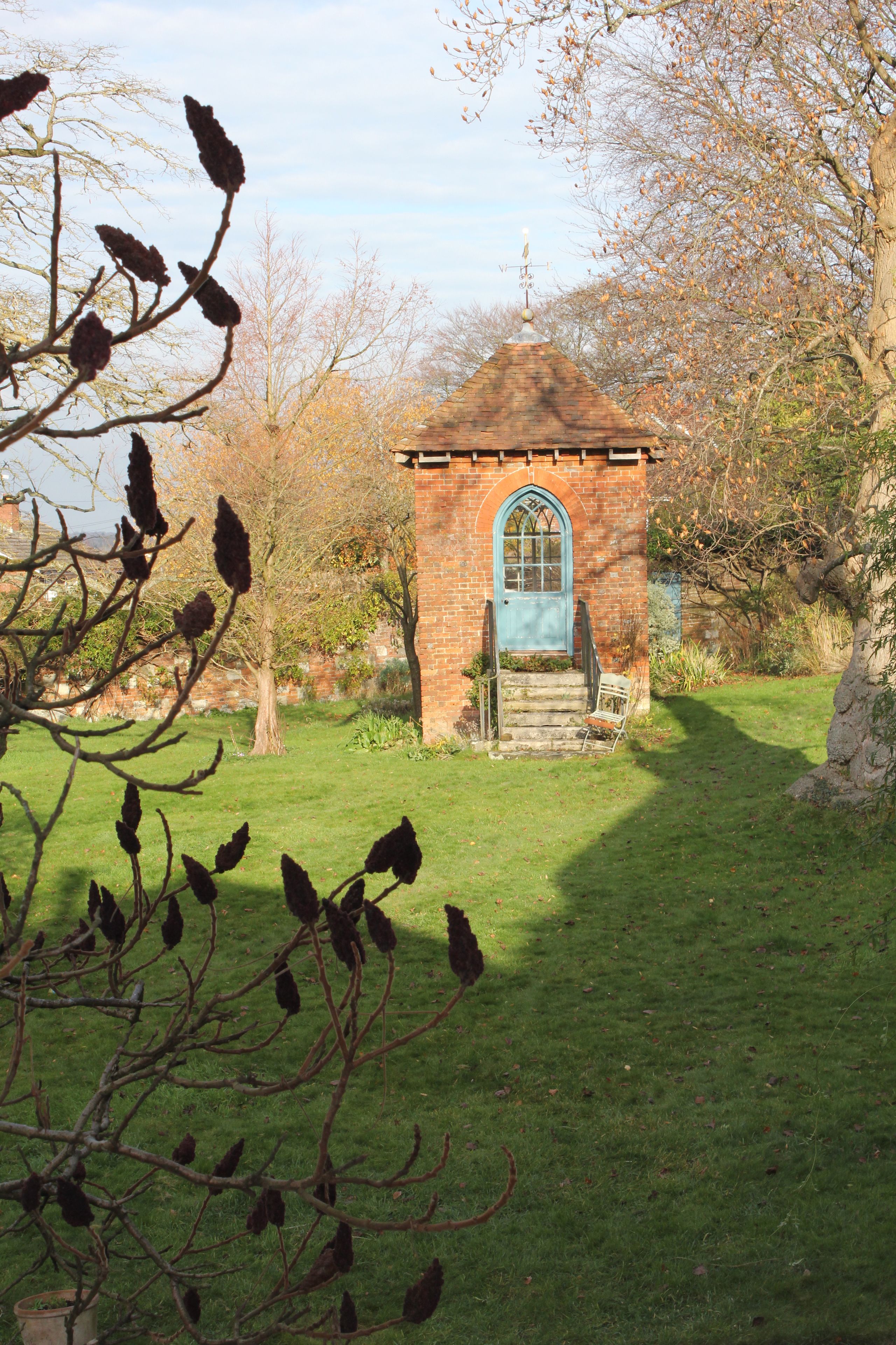 A small brick building with a blue door and steps leading up to it, surrounded by trees and grass.