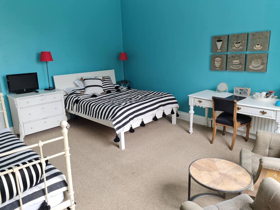A bedroom with a bed, a desk, a chair, a TV, and a coffee table.