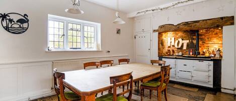 Une salle à manger avec une grande table et des chaises, une cuisine avec une pancarte indiquant « CUISINE » et une fenêtre donnant sur un beau paysage.