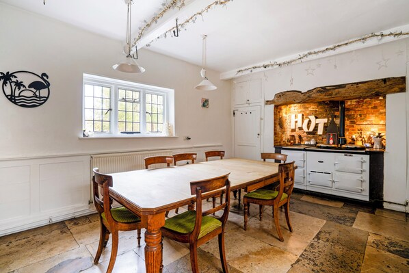 A dining room with a large table and chairs, a kitchen with a 'HOT' sign, and a window with a view. - St John's Croft (Winchester)