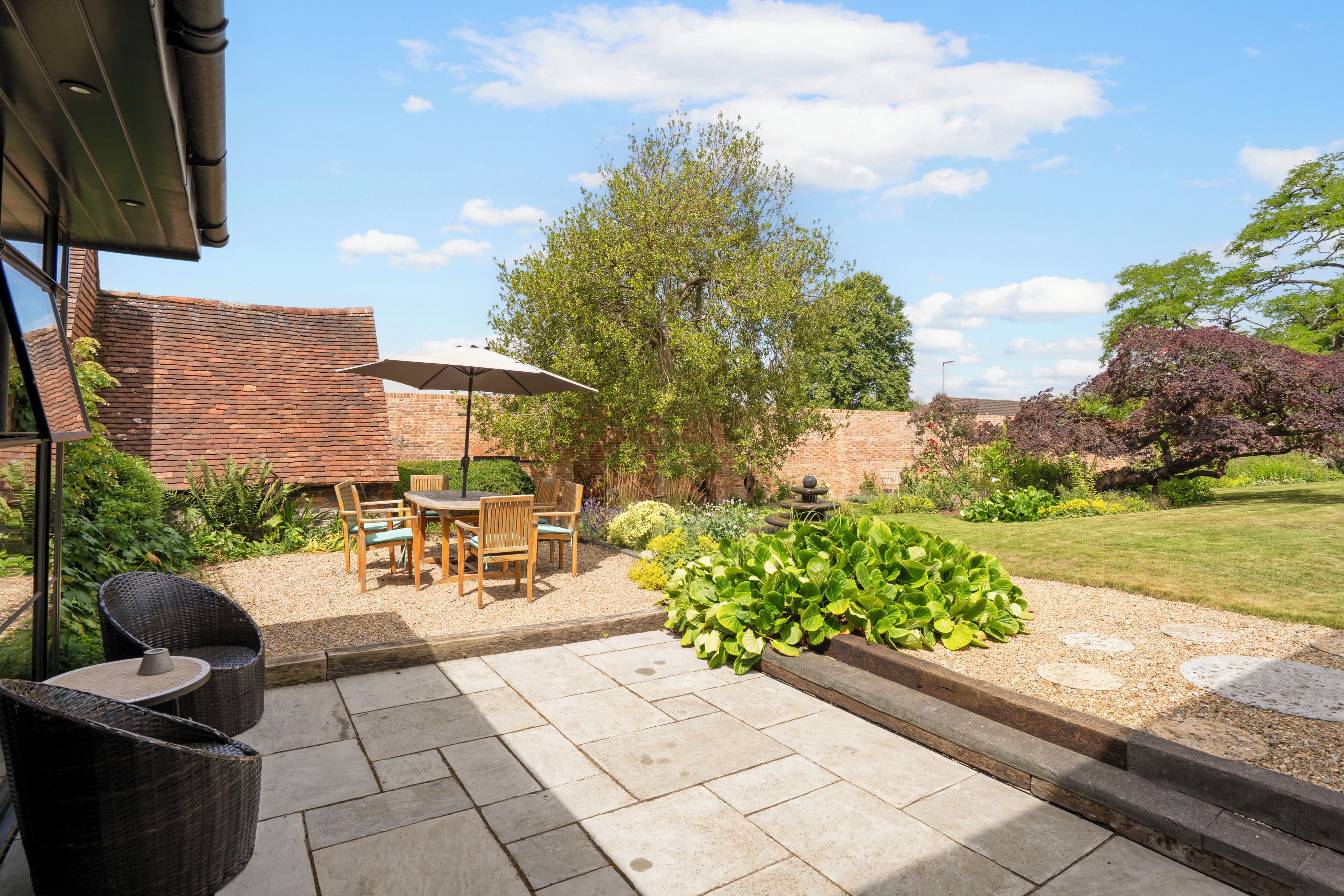 A patio with a table and chairs, a brick wall, and a garden with various plants.