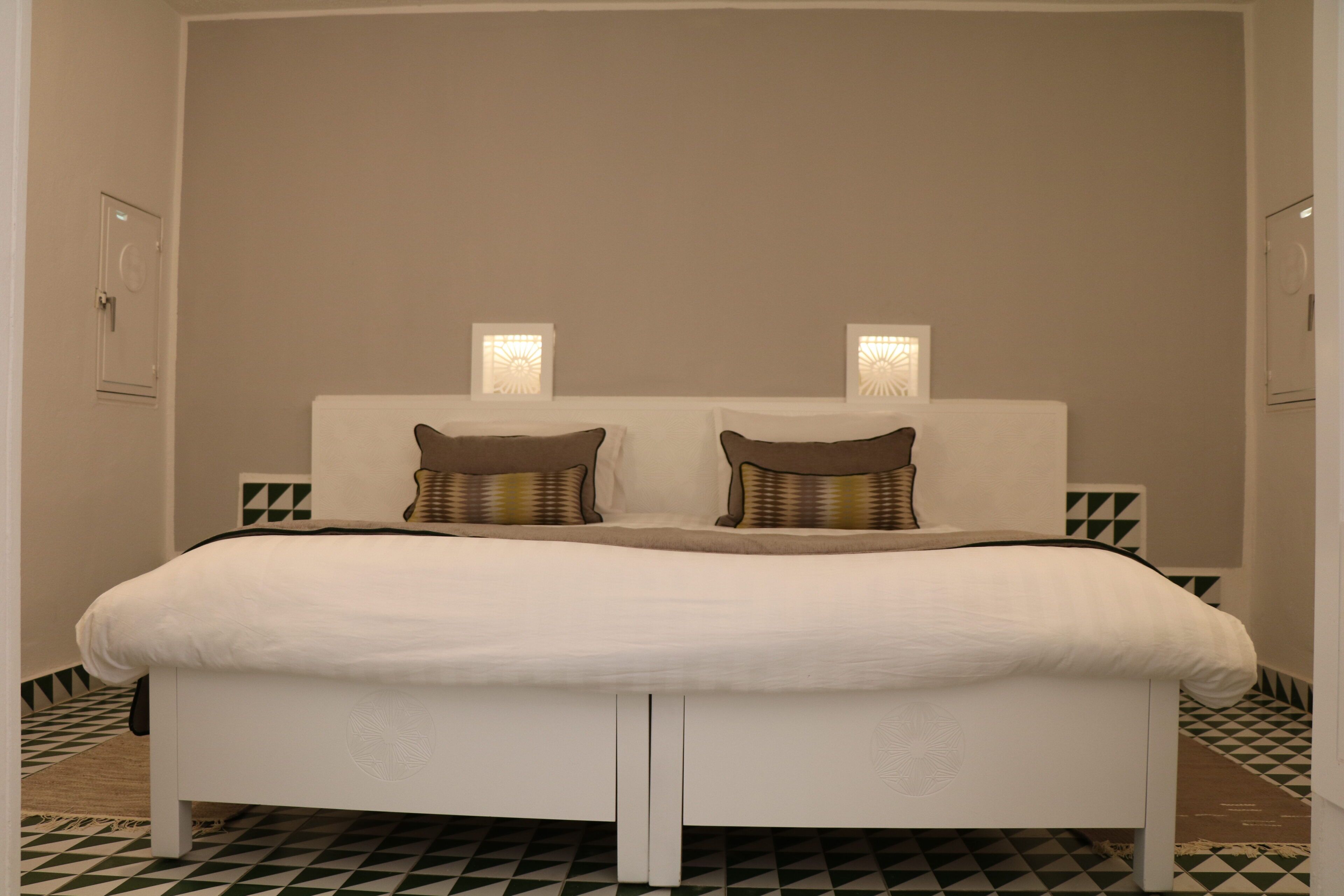 Cama com cabeceira branca, duas almofadas e luminárias de cabeceira.