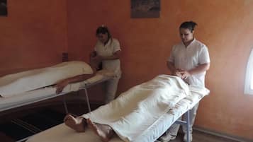 A room with two beds, one occupied by a person lying on a bed, and another person standing beside it.