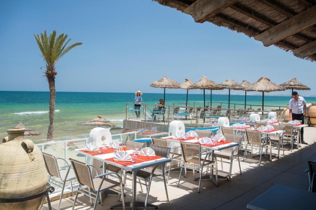 Area pranzo all'aperto con tavoli e sedie, una palma e vista sull'oceano.