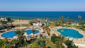 Un resort con varias piscinas, palmeras y vista al mar.