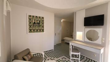 Une pièce dotée d’un sol à motifs géométriques, d’un canapé, d’une petite table, d’un téléviseur fixé au mur et d’une porte donnant sur une autre pièce.