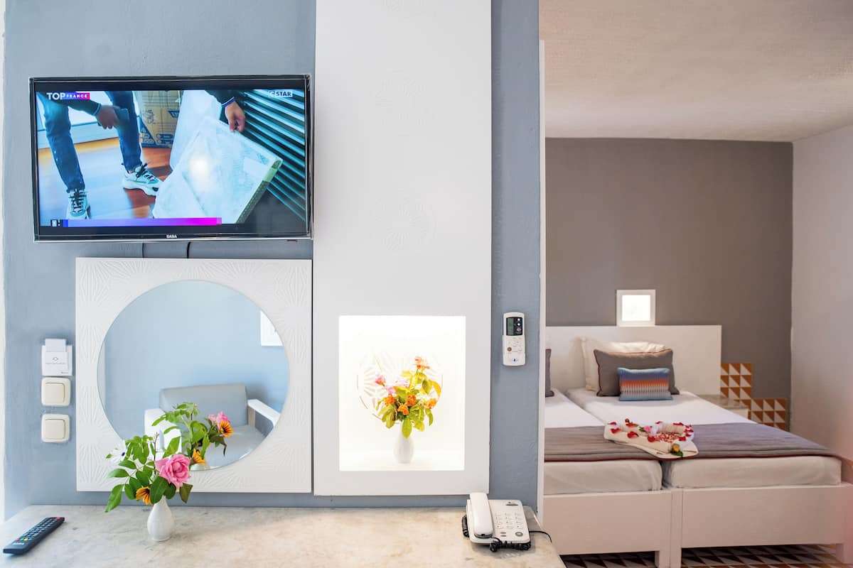Une chambre d’hôtel moderne avec un téléviseur fixé au mur, un lit avec une tête de lit blanche, une table de chevet avec un téléphone et un miroir décoratif.