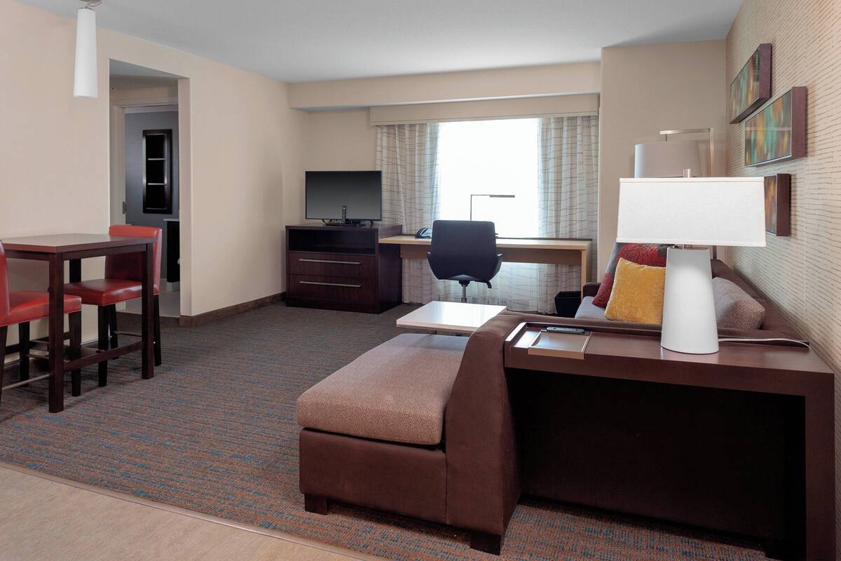 A hotel room with a desk, chair, TV, and a small sofa.