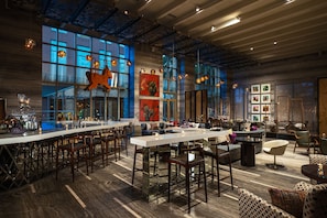 A spacious bar area with a long counter, multiple seating options including bar stools and sofas, and large windows providing natural light. - Renaissance Bengaluru Race Course Hotel (Bengaluru)