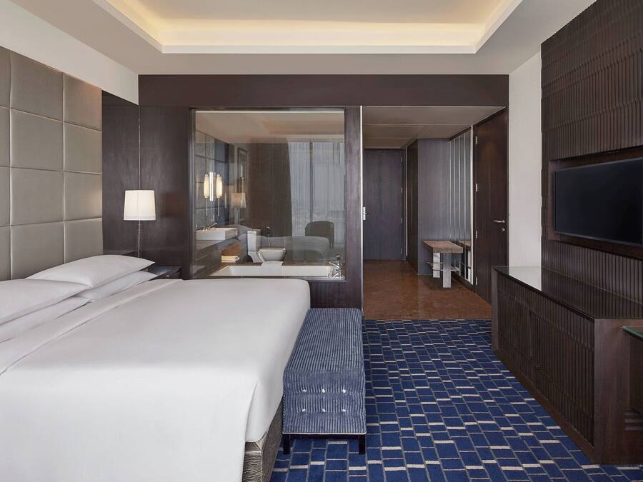 A hotel room with a large bed, a seating area, a TV, and a bathroom visible through an open door.