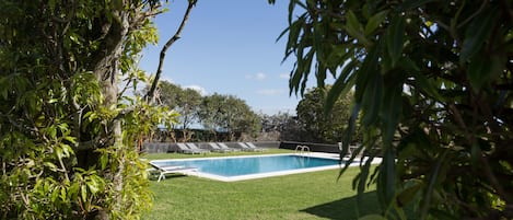 Una piscina al aire libre, sombrillas, sillones reclinables de piscina