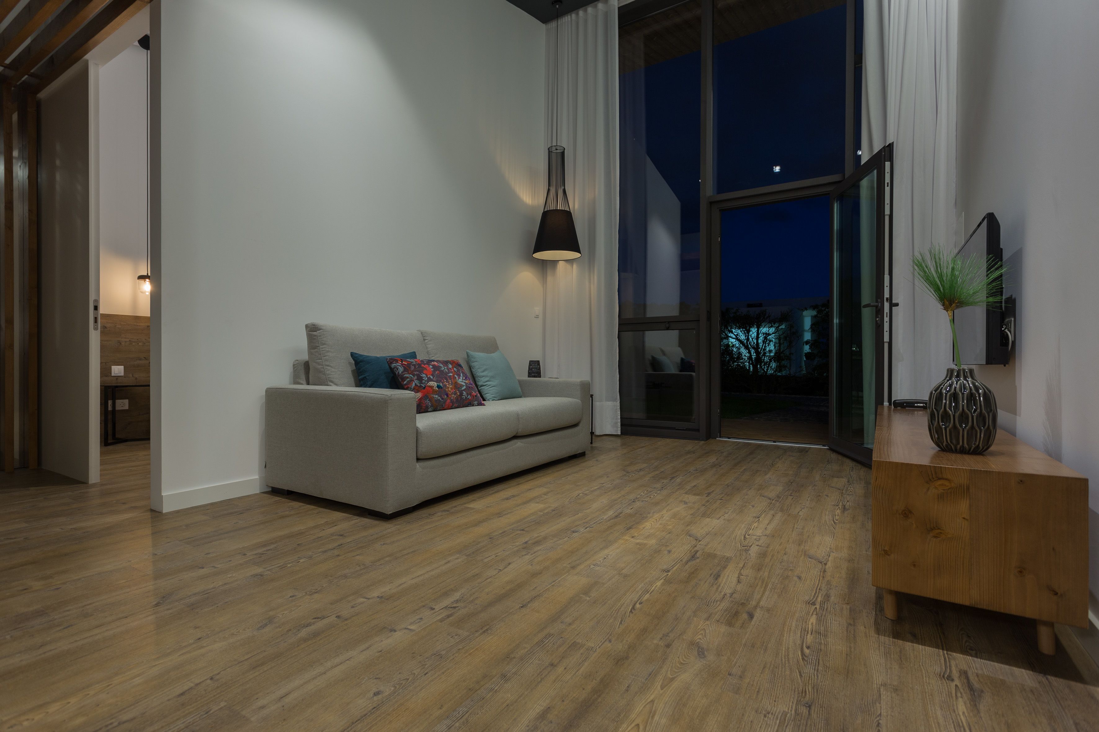A modern living room with a sofa, a wooden side table, and a large window.