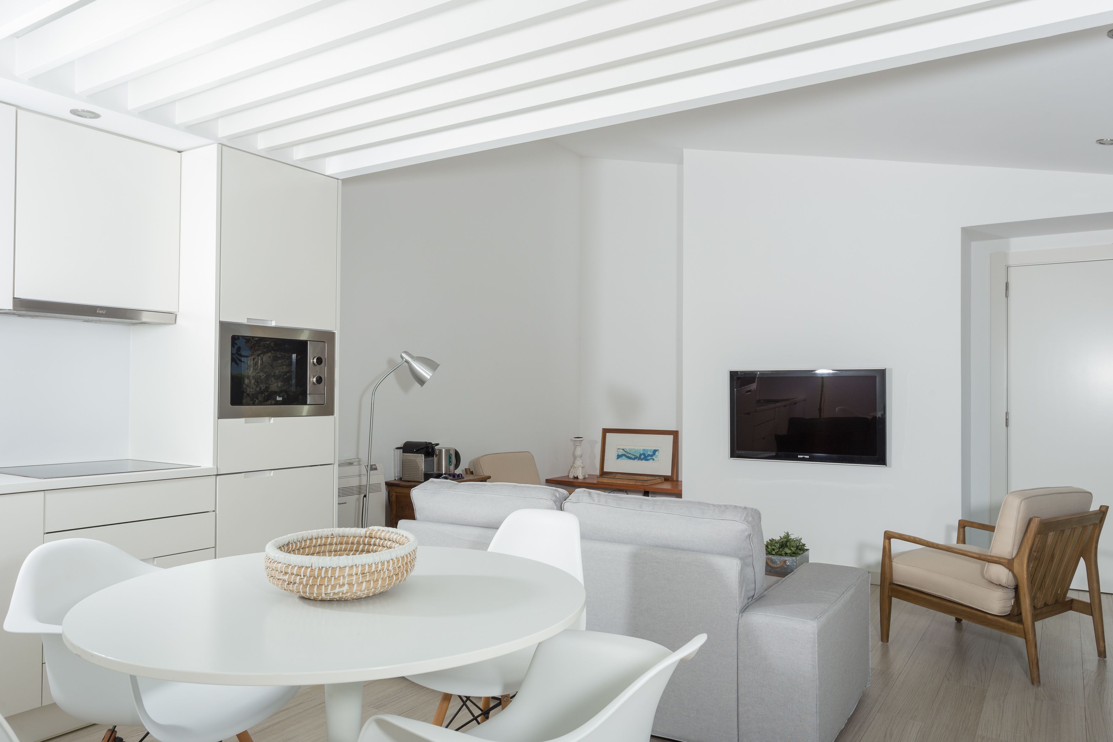 A modern living room with a white sofa, a round dining table, and a television mounted on the wall.