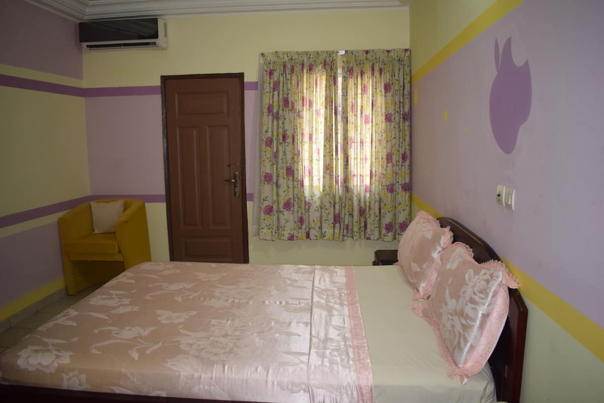 A bedroom with a bed, a chair, a door, and a window with curtains.