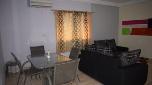 A living room with a black sofa, patterned cushions, a dining table with chairs, and a curtain with a geometric design. - Hôtel Résidence Péronne (Abidjan)