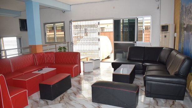 A spacious living area with a red sofa, black leather sofa, and ottoman, a coffee table, and a TV. - Hôtel Résidence Péronne (Abidjan)