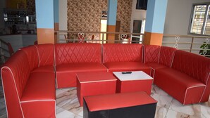 A red sectional sofa with a black ottoman, a small table, and a heart-shaped railing in a room with patterned wallpaper and a tiled floor. - Hôtel Résidence Péronne (Abidjan)