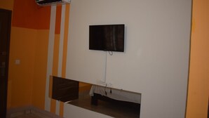 A room with a mounted TV, an air conditioning unit, and a small table with a tablecloth. - Hôtel Résidence Péronne (Abidjan)