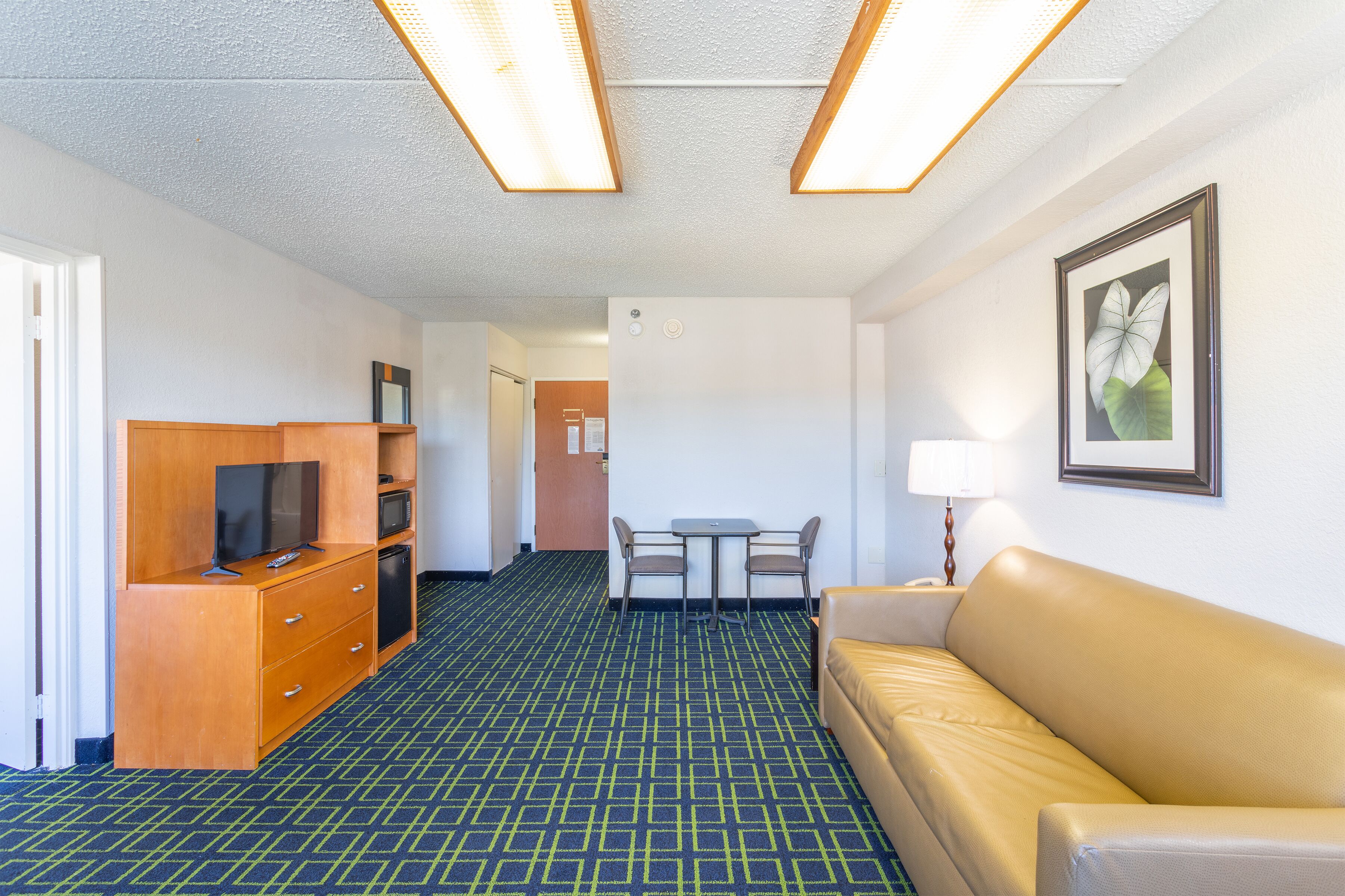 A hotel room with a kitchenette, a sofa, a dining table with chairs, and a framed picture on the wall.