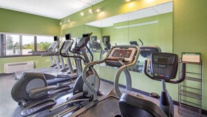 Een sportschool met loopbanden, elliptische trainers en een gewichtbank.