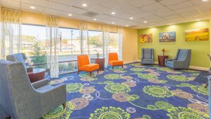 Een hotel lobby met een blauw patroon tapijt, verschillende stoelen, een kleine tafel met een vaas en kunstwerken aan de muren.