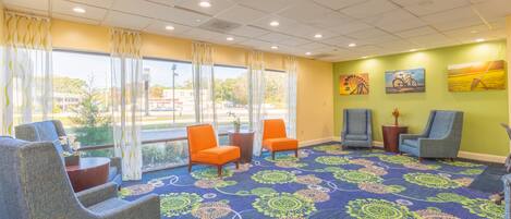 A hotel lobby with a blue patterned carpet, several chairs, a small table with a vase, and artwork on the walls.