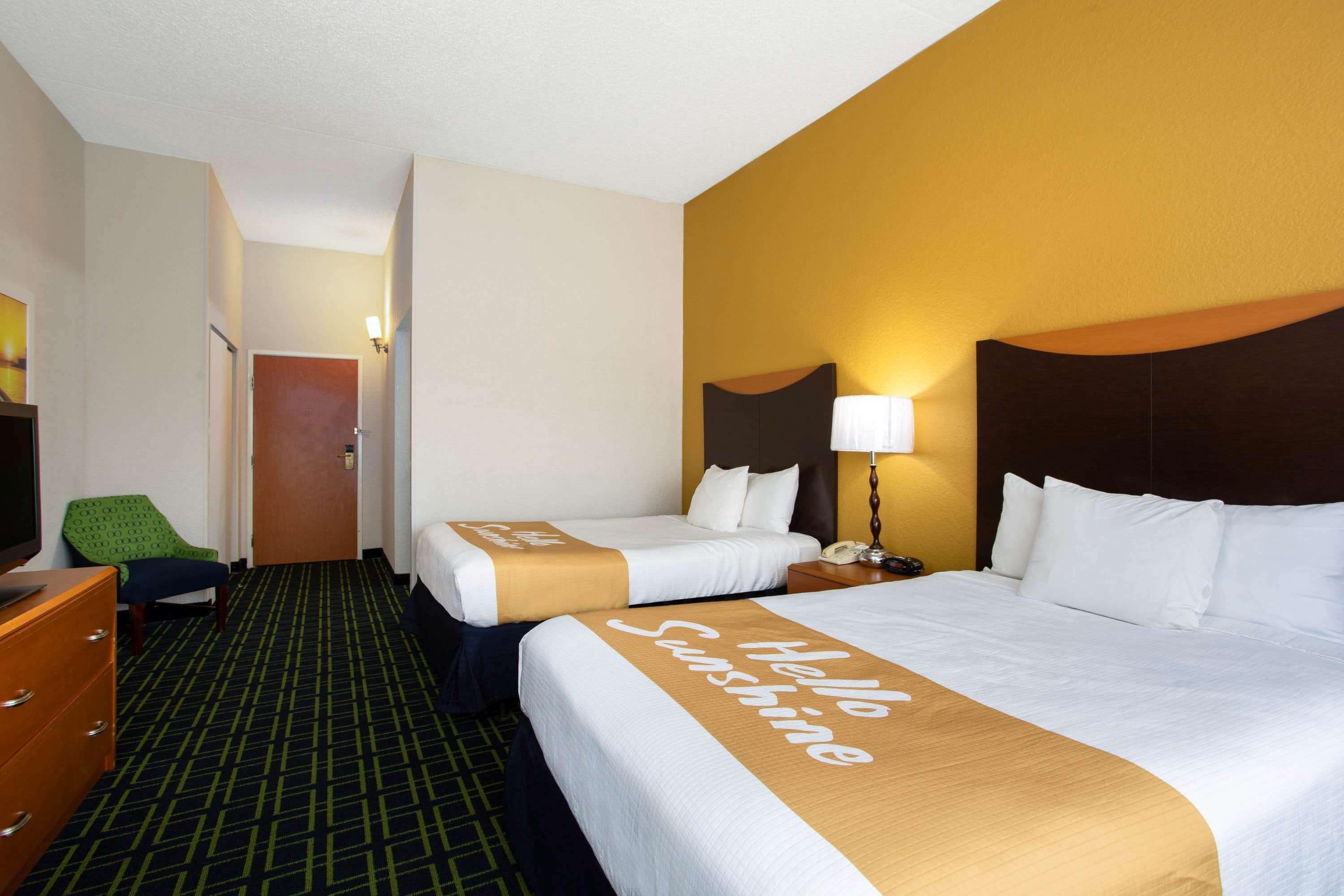 Habitación de hotel con dos camas, una silla verde, un aparador y una lámpara.