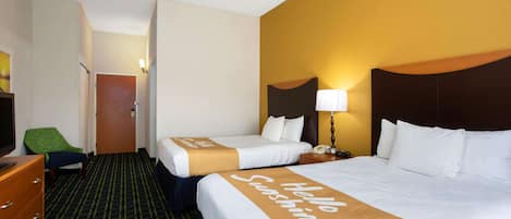 Habitación de hotel con dos camas, una silla verde, un aparador y una lámpara.