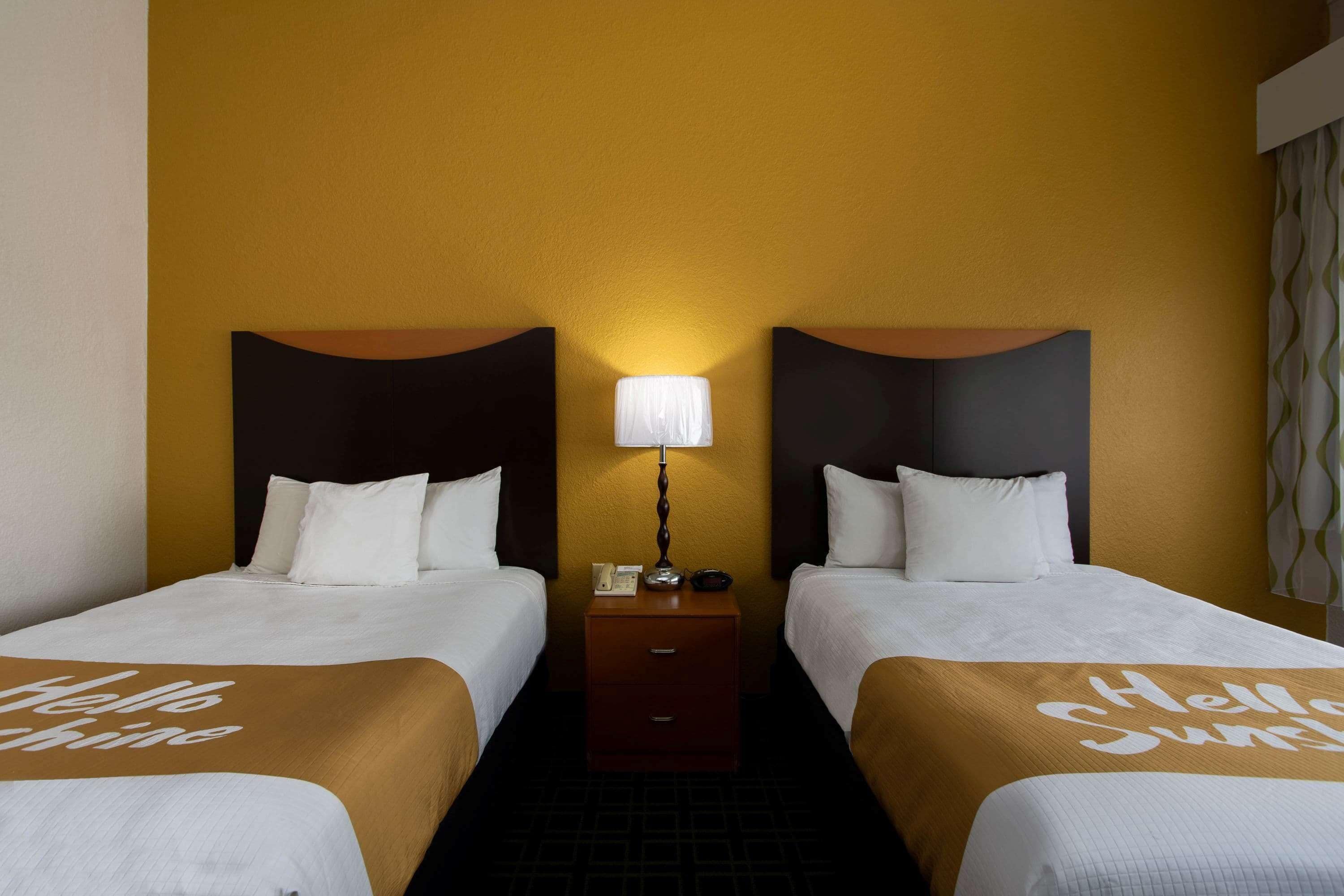 Habitación de hotel con dos camas, cada una con cabecero, una mesita de noche entre ellas y una lámpara.