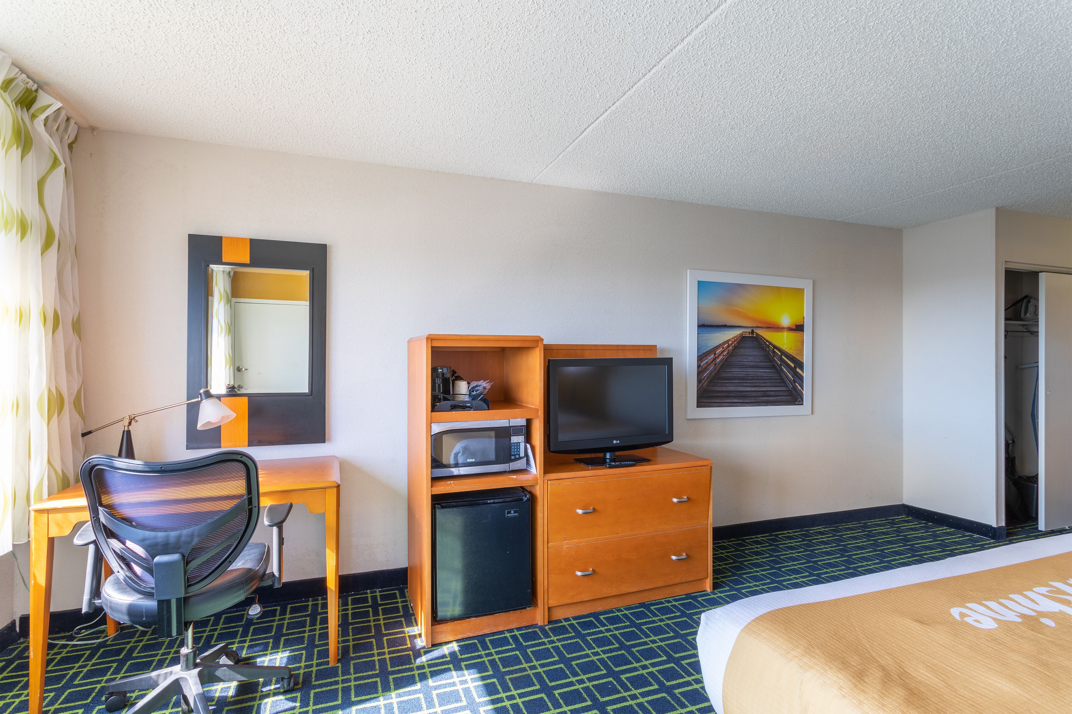 Ein Hotelzimmer mit Bett, Schreibtisch, Computer, Stuhl, Mikrowelle und Fernseher.