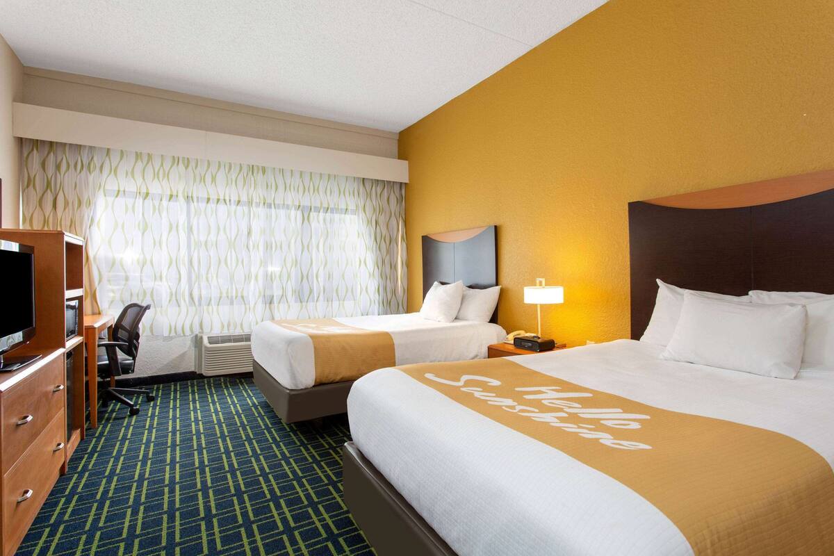 Une chambre d’hôtel avec deux lits, un bureau avec une chaise, une télévision et une fenêtre avec des rideaux.