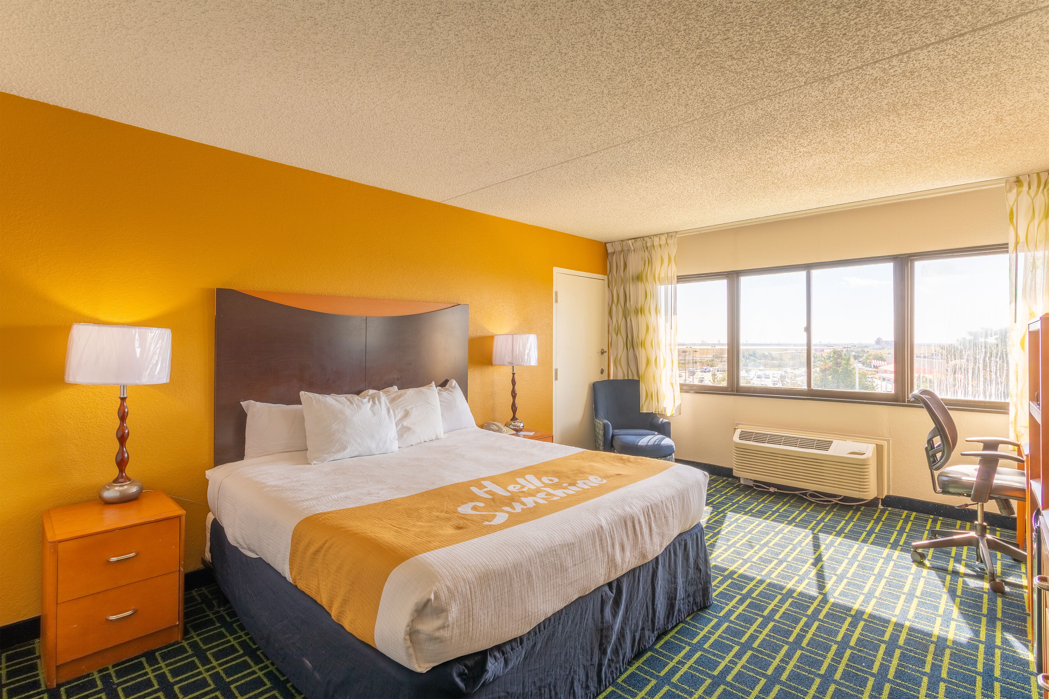 A hotel room with a large bed, two bedside lamps, a view of the city, and a window with curtains.