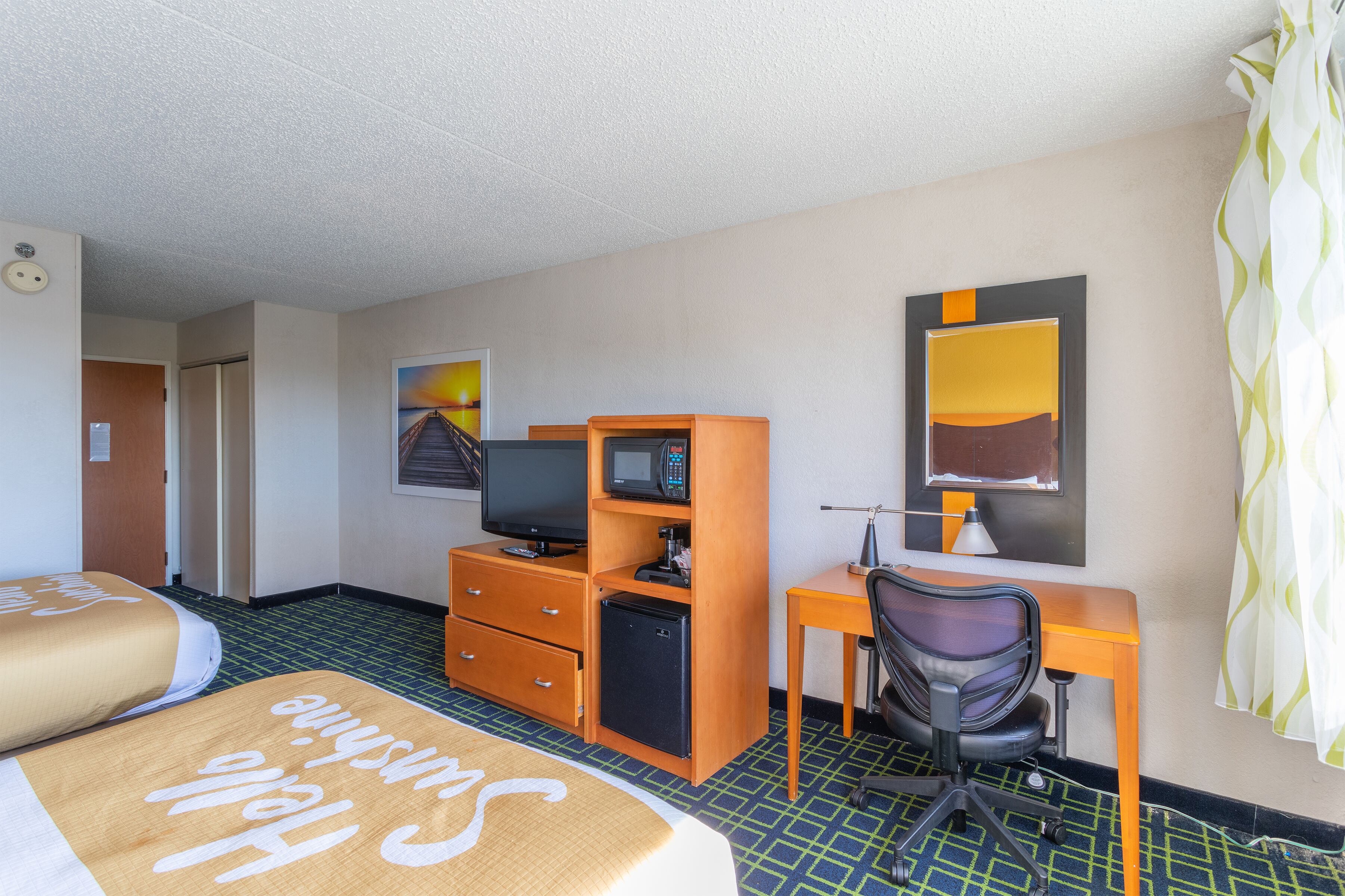 Habitación de hotel con dos camas, un escritorio con computadora, un refrigerador pequeño y una televisión.