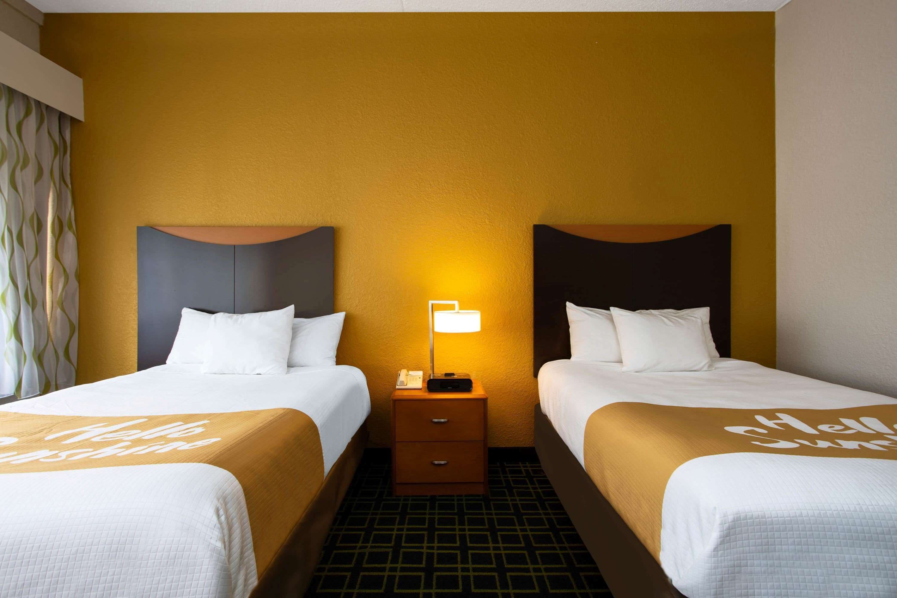 Ein Hotelzimmer mit zwei Betten, einem Nachttisch mit Lampe und einem gemusterten Boden.
