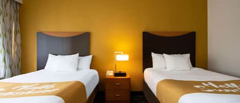 A hotel room with two beds, a nightstand with a lamp, and a patterned floor.