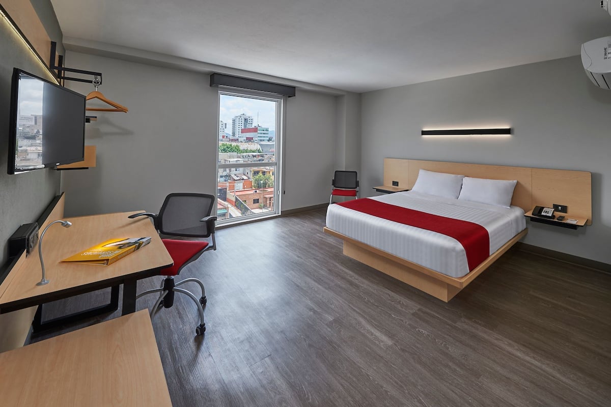 A modern hotel room with a bed, desk, chair, and a TV.