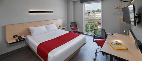 A modern hotel room with a large bed, a desk, a chair, a TV, and a window with a city view.