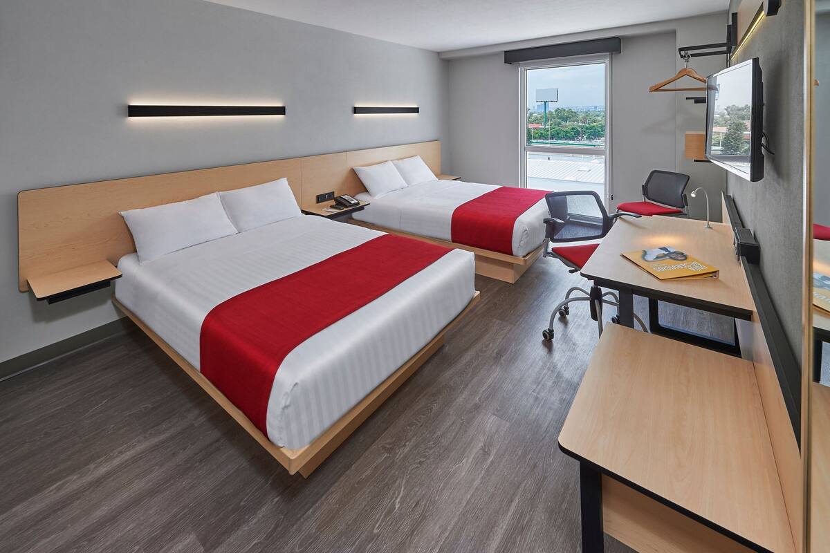 A hotel room with two beds, a desk, a chair, a TV, and a window with a city view.