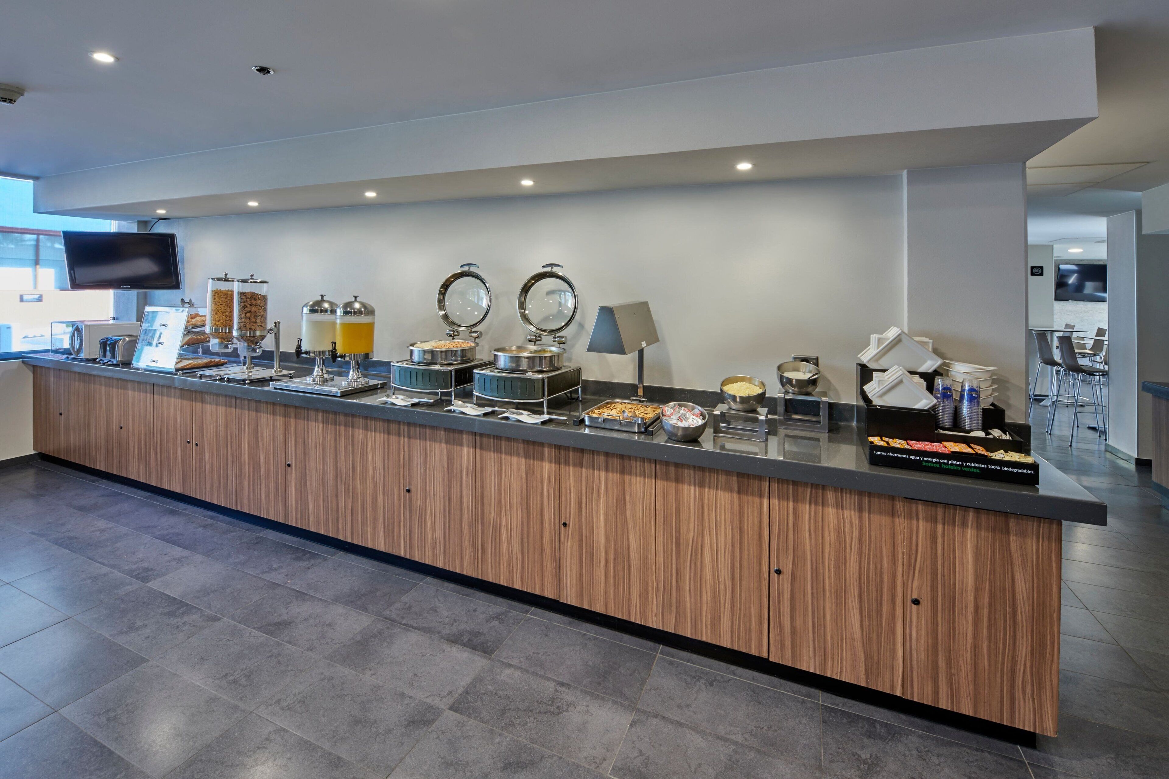 Una barra de desayuno moderna con detalles de madera, equipada con varios dispensadores de alimentos y un televisor de pantalla plana.