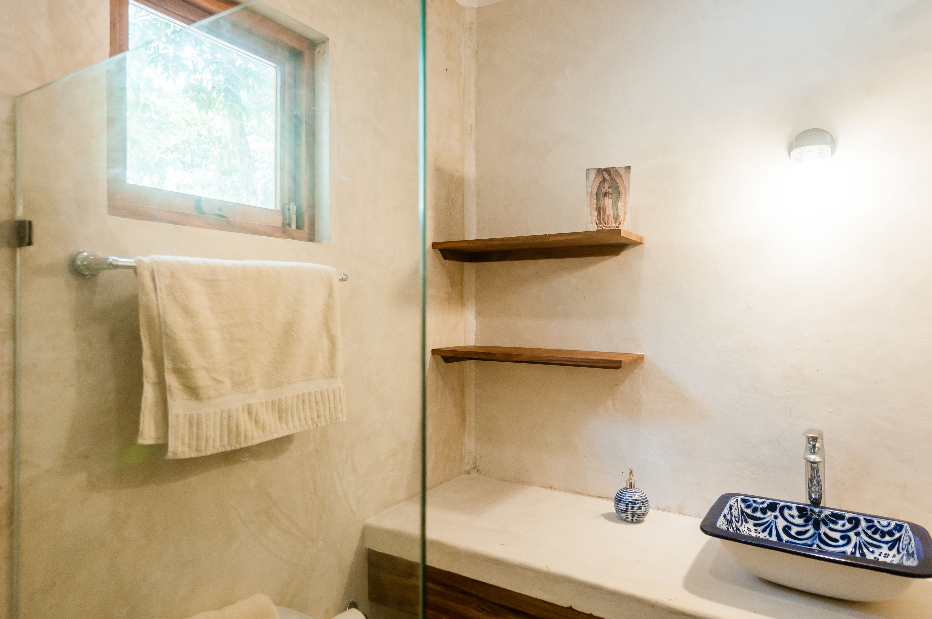 A bathroom with a glass shower enclosure, a white sink with a blue and white patterned basin, and two wooden shelves.