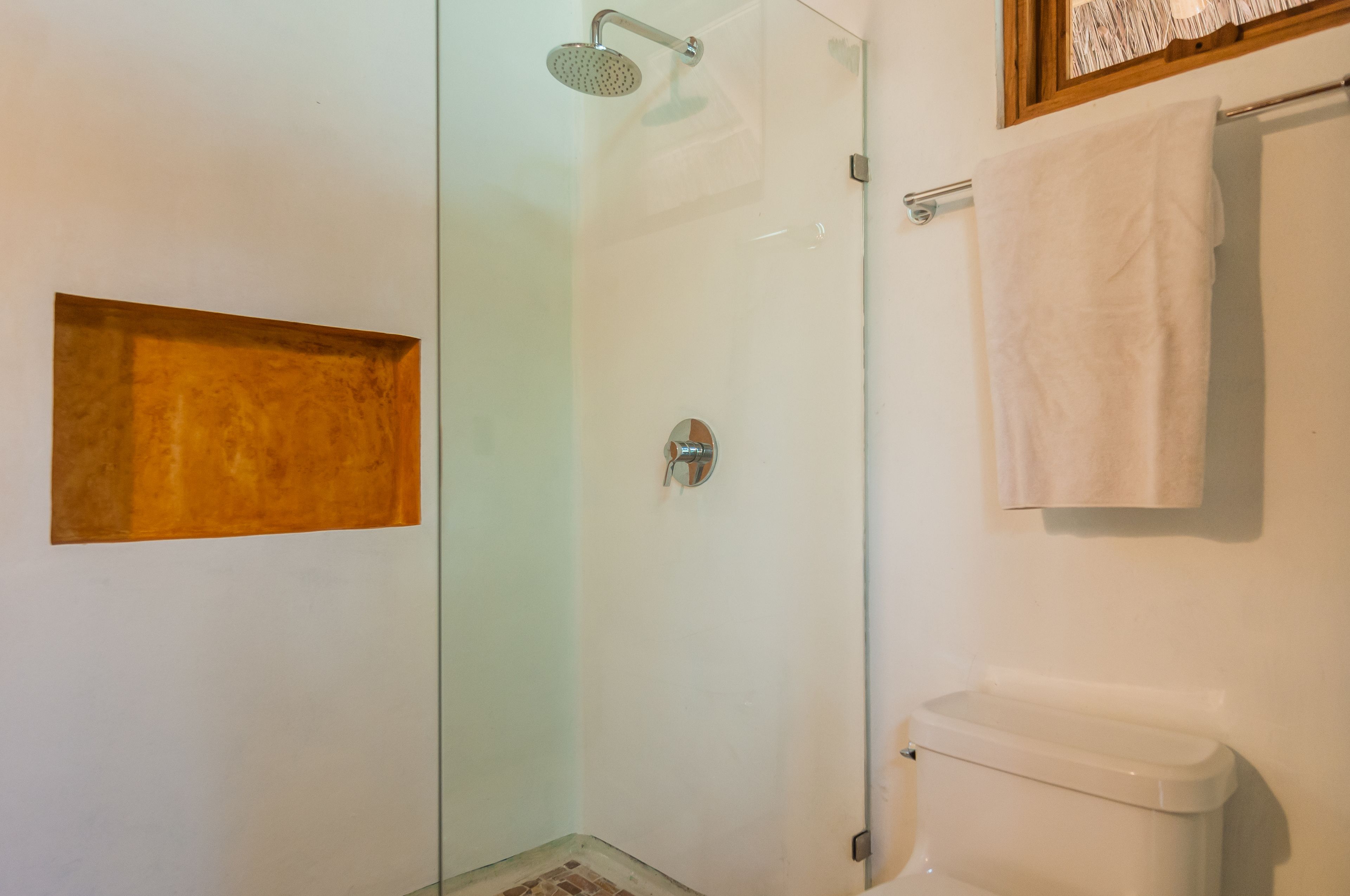 A bathroom with a glass shower enclosure, a white toilet, and a towel hanging on a rack.