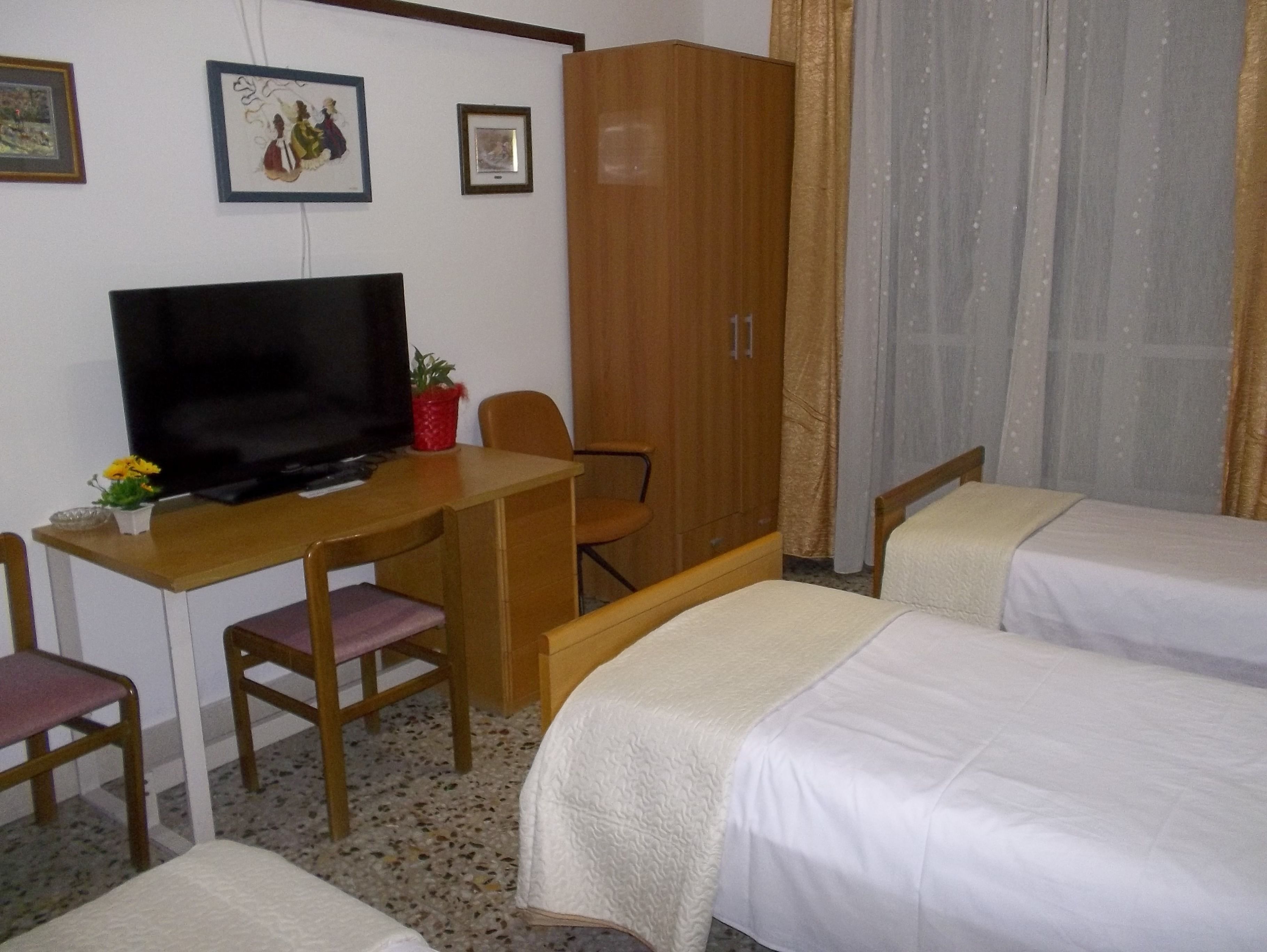 A hotel room with a bed, a desk with a TV, a chair, and a wardrobe.