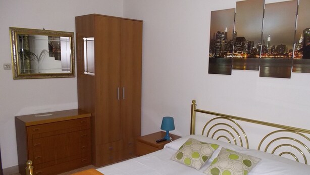 Habitación de hotel con cama, armario de madera, mesita de noche con lámpara, vista a la ciudad y espejo en la pared.