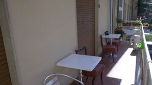 Un balcón con mobiliario exterior, incluyendo sillas y mesas de metal, y plantas en macetas.