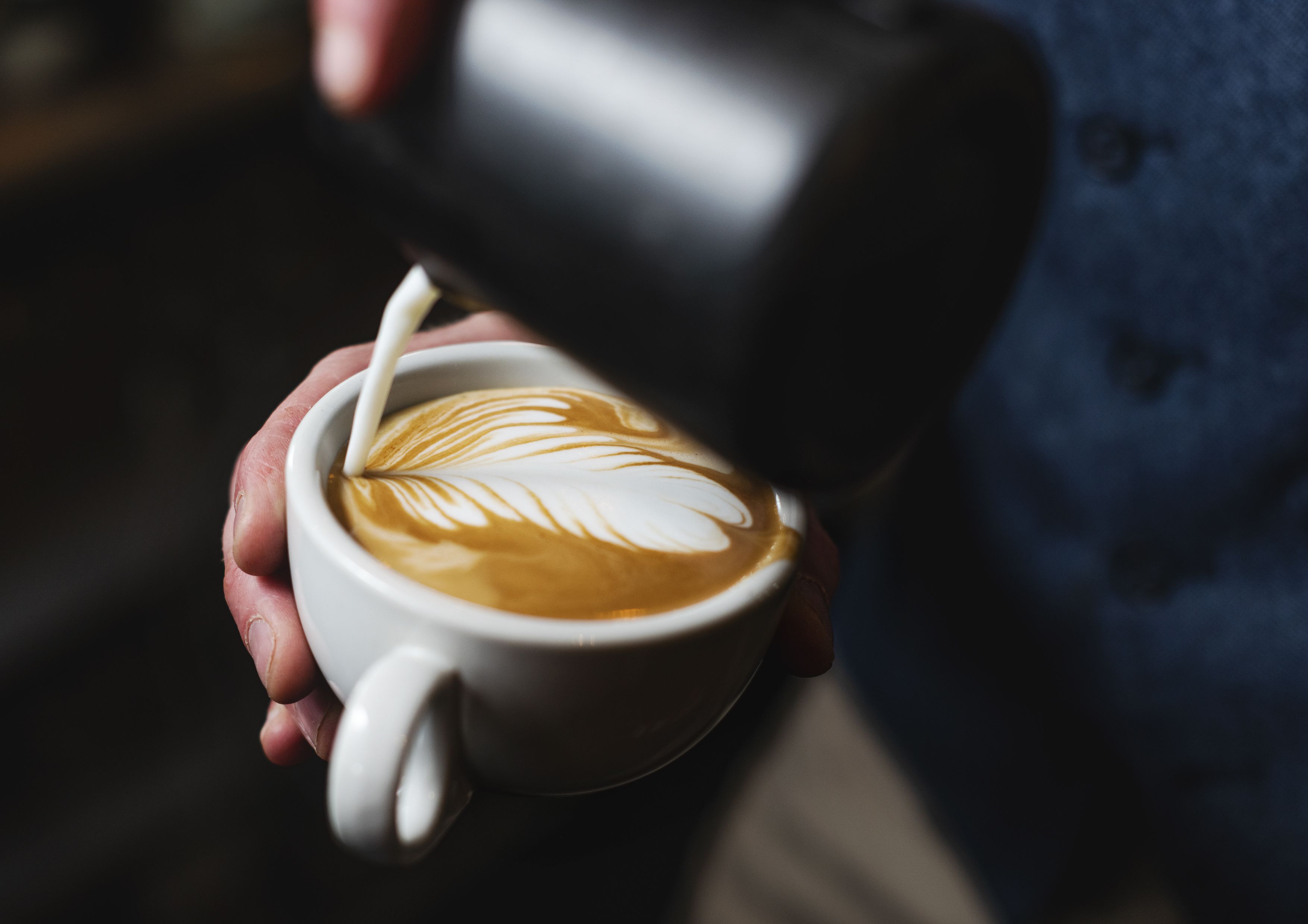 A person holding a cup of coffee with latte art.