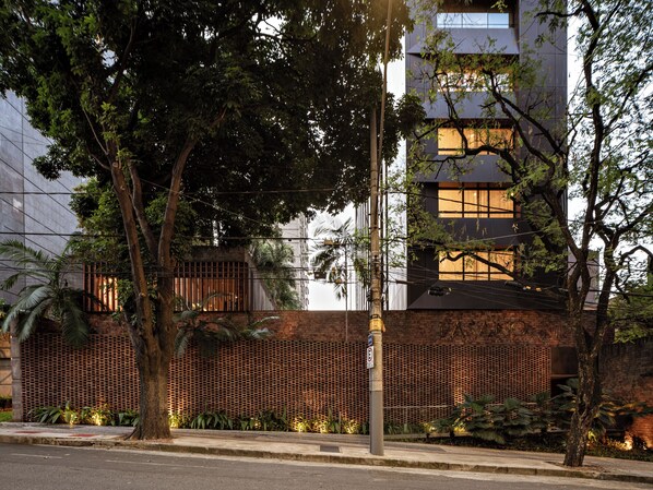 A modern building with a brick facade, large windows, and a tree-lined street.