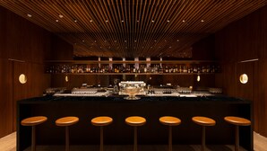 A bar area with a central bar counter, multiple stools, and shelves stocked with bottles.